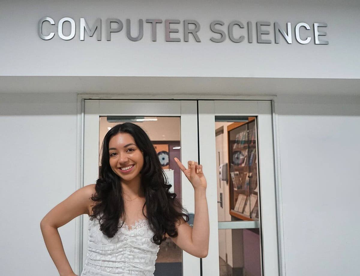 Adriana holding her graduation gown with Computer Science written in the background